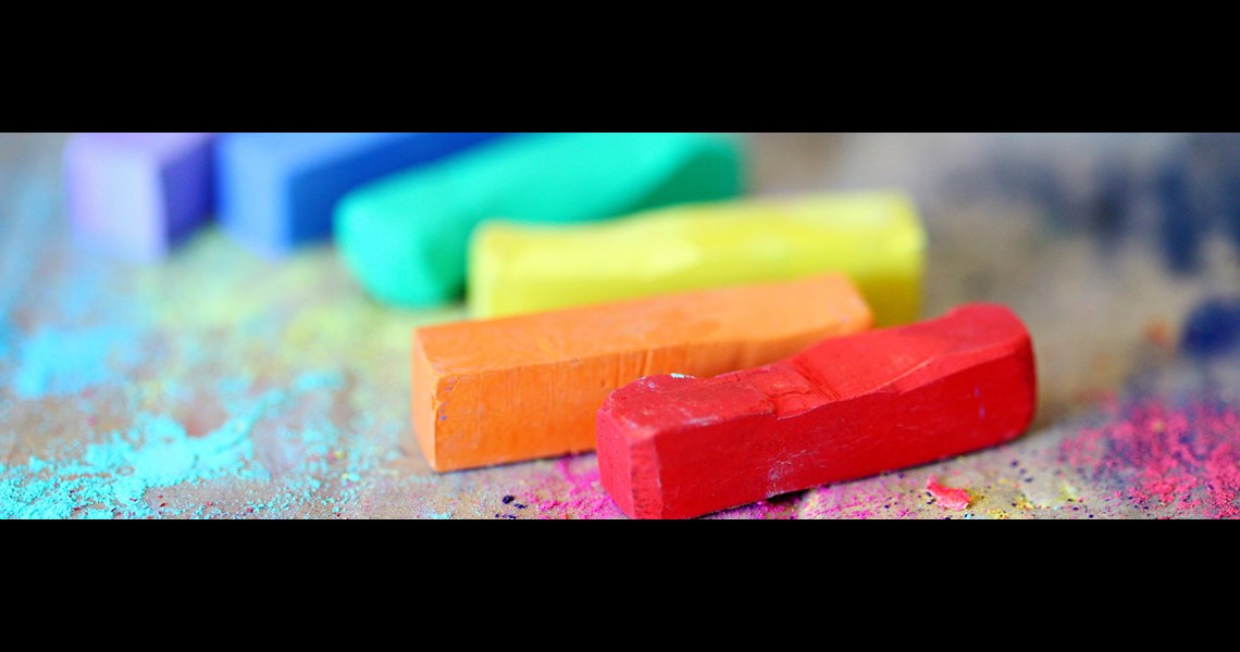 A decorative image of rainbow coloured chalks resting on a wooden surface